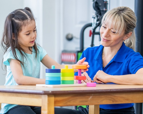 a girl playing with a stack of colorful toys with a speech therapist