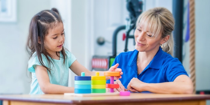 a girl playing with a stack of colorful toys with speech therapist