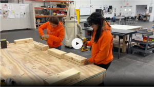 The Lopez sisters wear orange Easterseals Redwood hoodies and work on a construction project in the Construction Lab